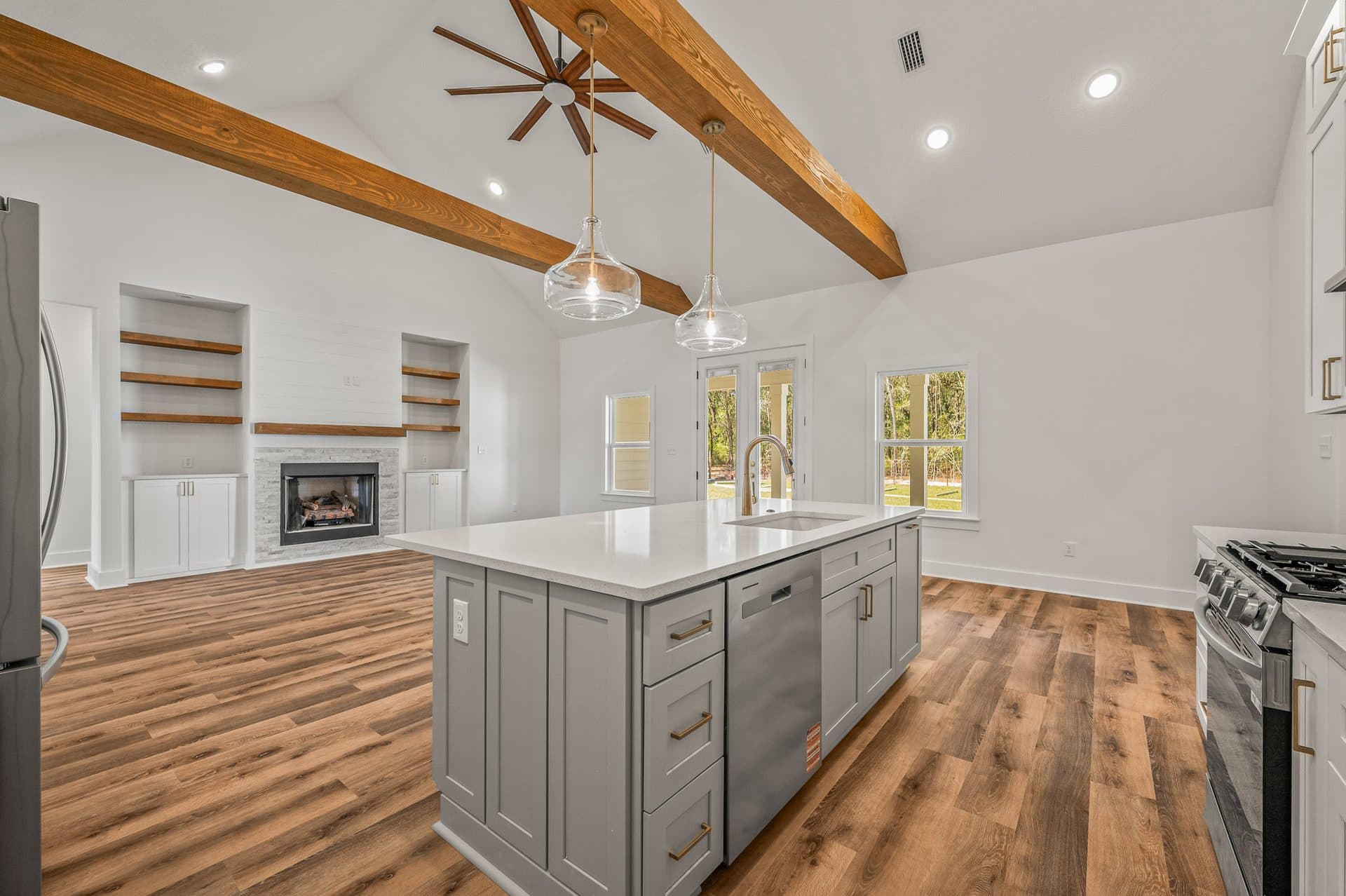Looking across the Cameron's grey kitchen island to the fireplace wall and French doors under the beamed ceiling